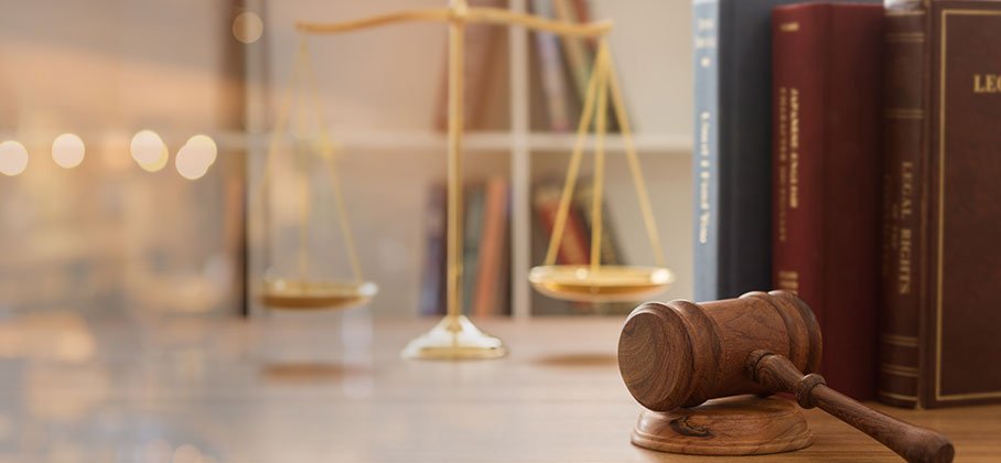 A gavel in focus in front of a set of gold scales